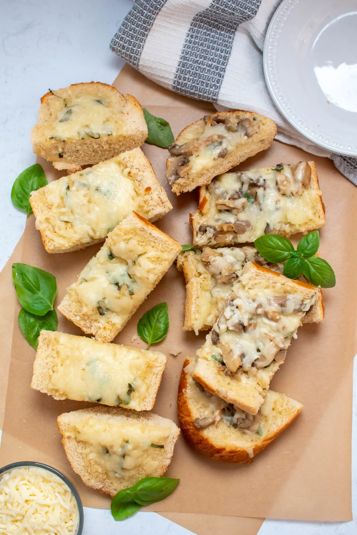 Pieces of cheesy bread with basil, mozzarella, and mushrooms, on brown parchment paper.