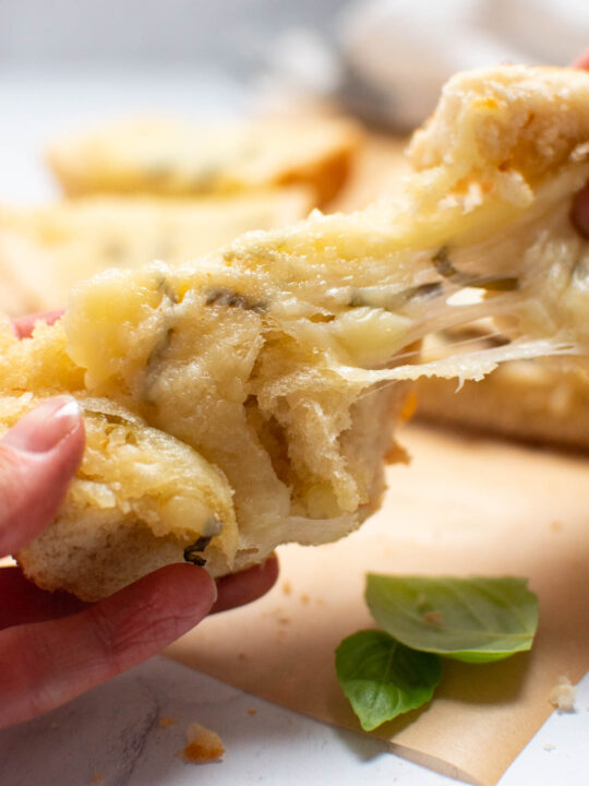 Woman pulls pieces of cheesy French bread apart.