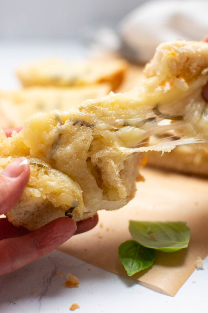 Woman pulls pieces of cheesy French bread apart.