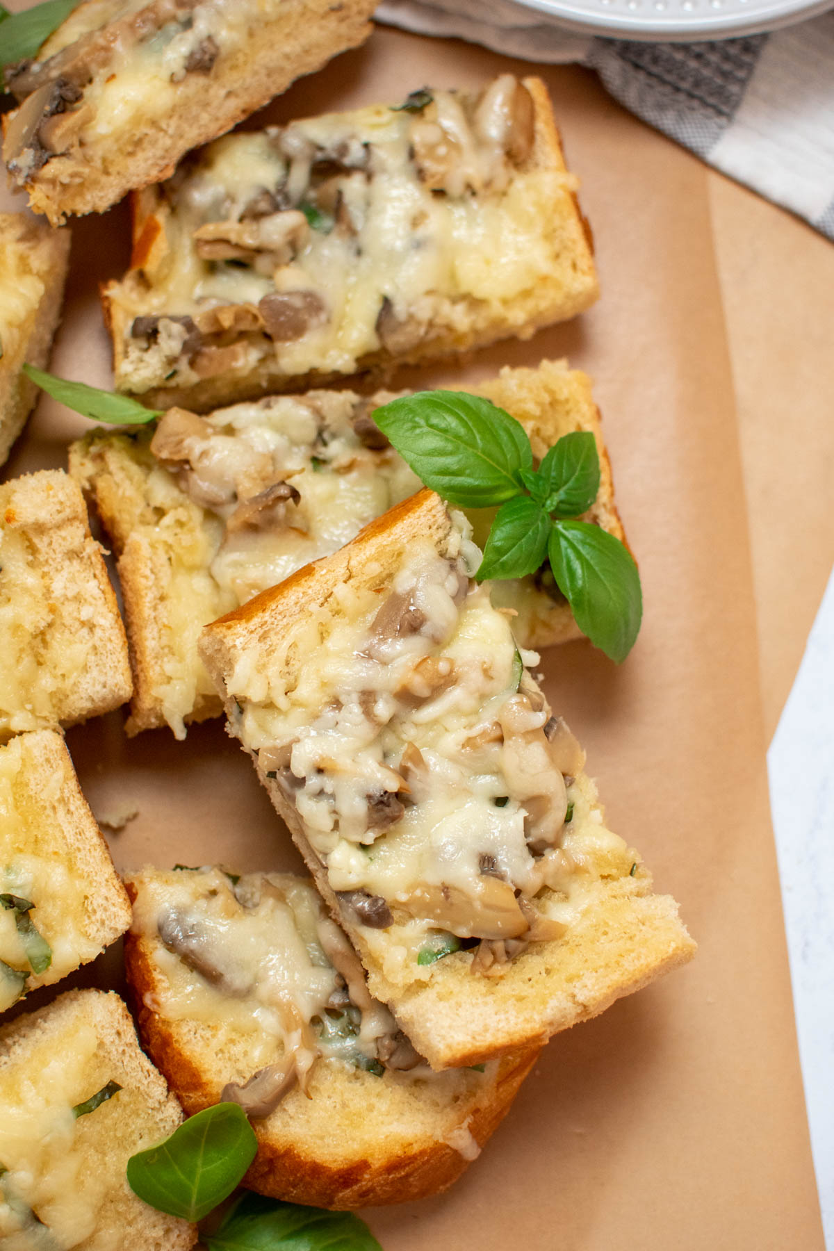 Pieces of cheesy mushroom bread garnished with fresh basil leaves on brown parchment paper.