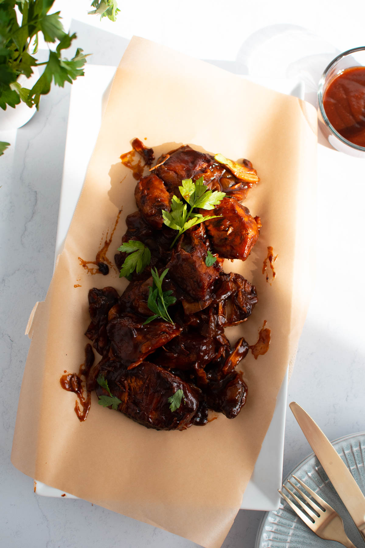 Country style ribs with barbeque sauce on brown parchment paper and garnished with fresh parsley.