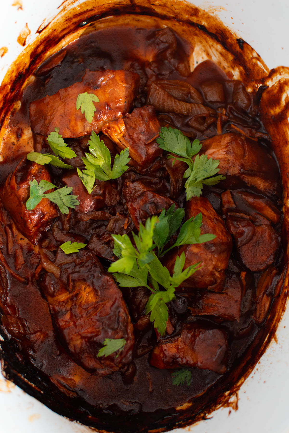Crock Pot ribs with barbeque sauce, onion slices, and parsley leaves.