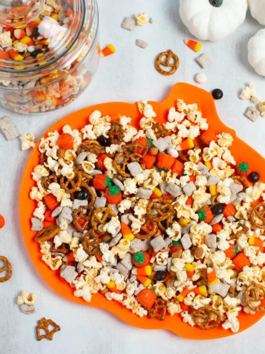 Halloween snack mix with popcorn, candy, and pretzels on orange pumpkin platter.