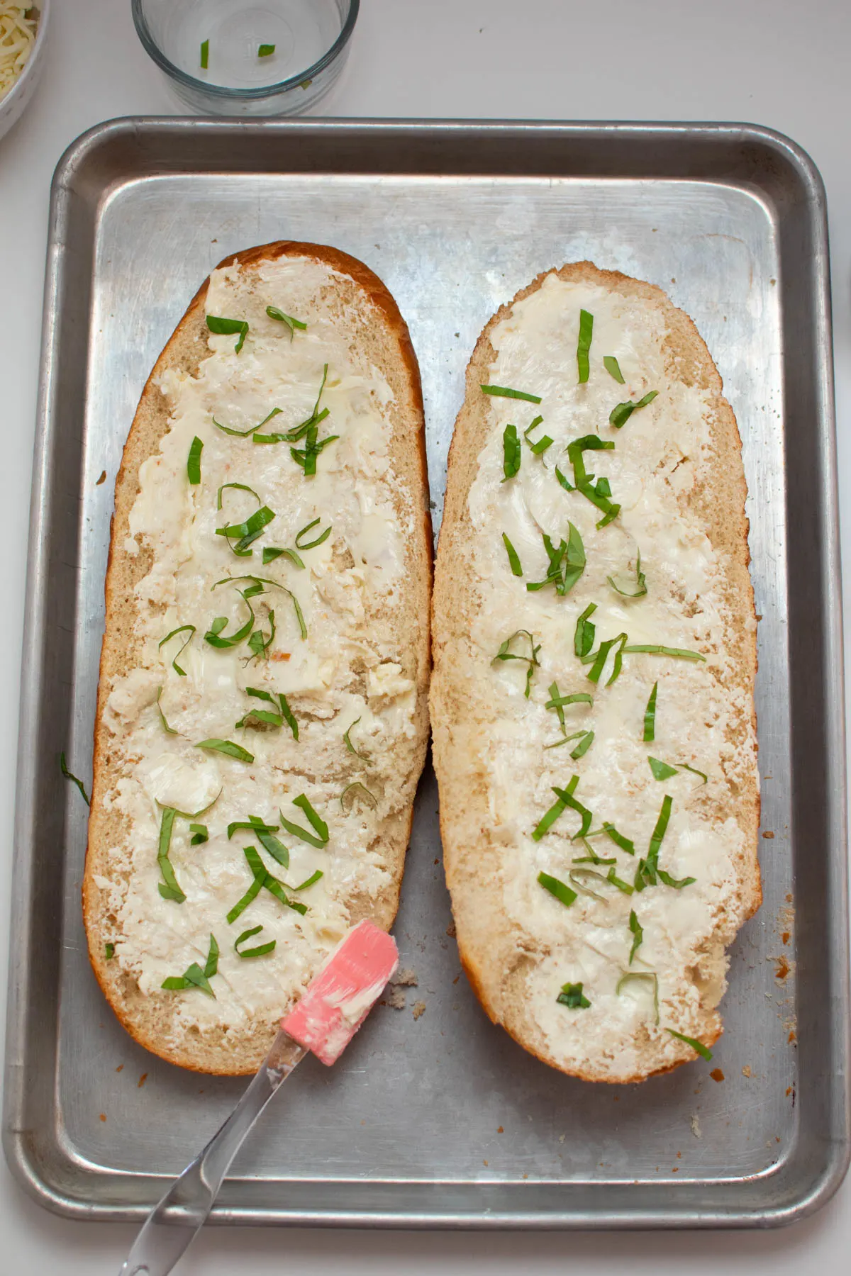 Two French bread halves with butter and basil ribbons on baking sheet.