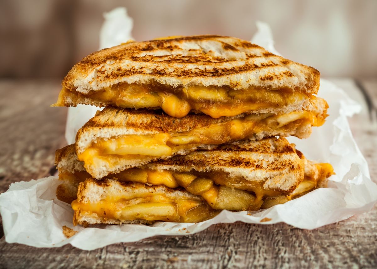Stack of three grilled cheese sandwich halves on a white cloth and brown kitchen table.