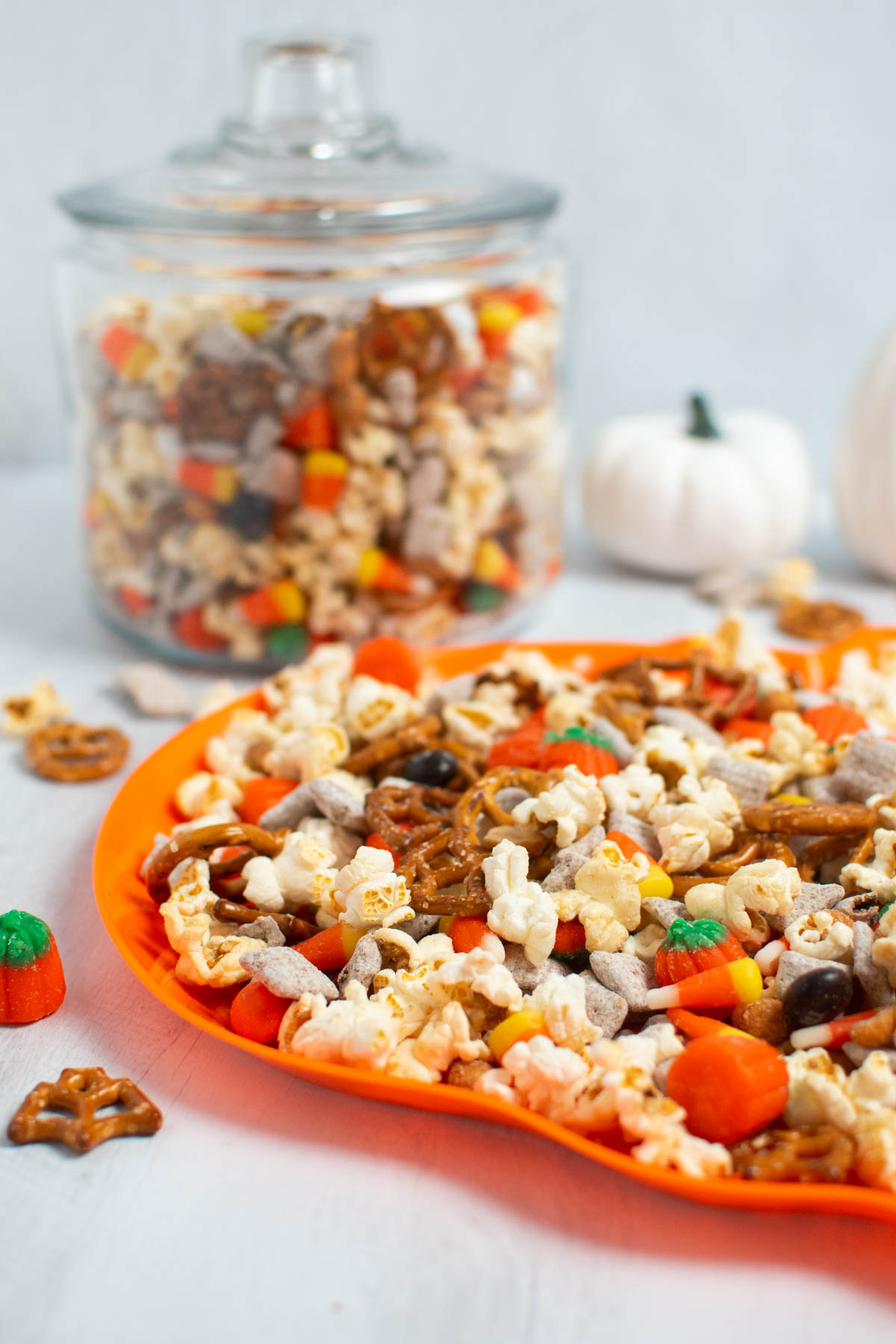 Halloween chex mix on orange pumpkin platter with jar of snack mix in background.