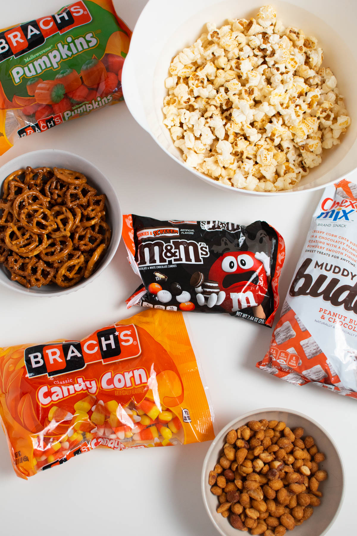 Bags and bowl of Halloween snack mix ingredients on white table.