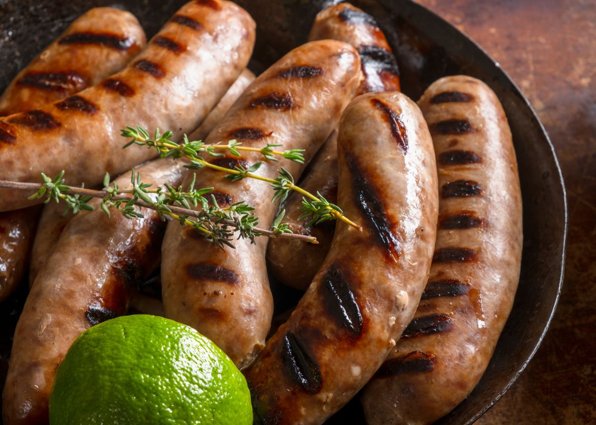 Several grilled sausage links on a black dish with green garnish and a wedge of lime.