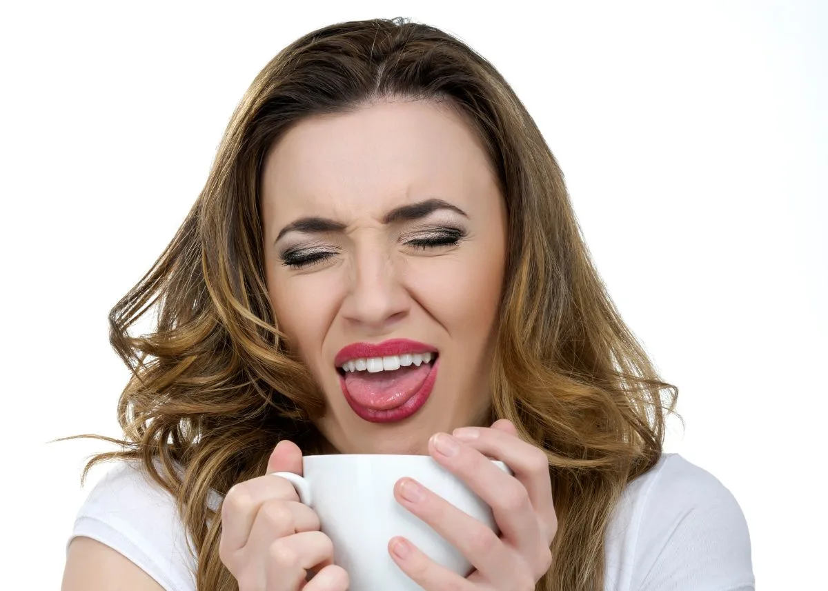 Woman makes a disgusted face after drinking from a small white mug.