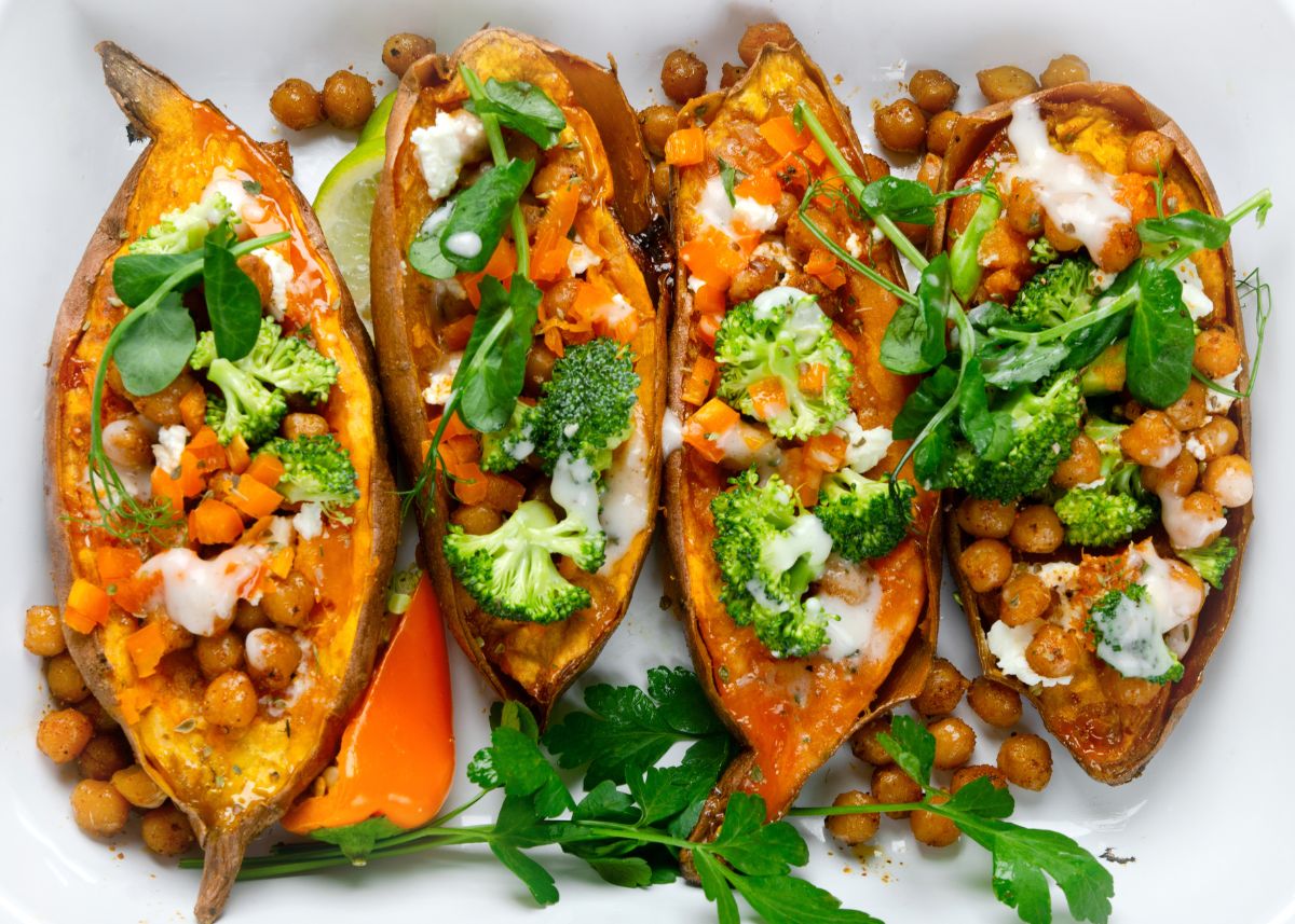 Several baked sweet potatoes filled with chickpeas, broccoli, and cilantro on white background.