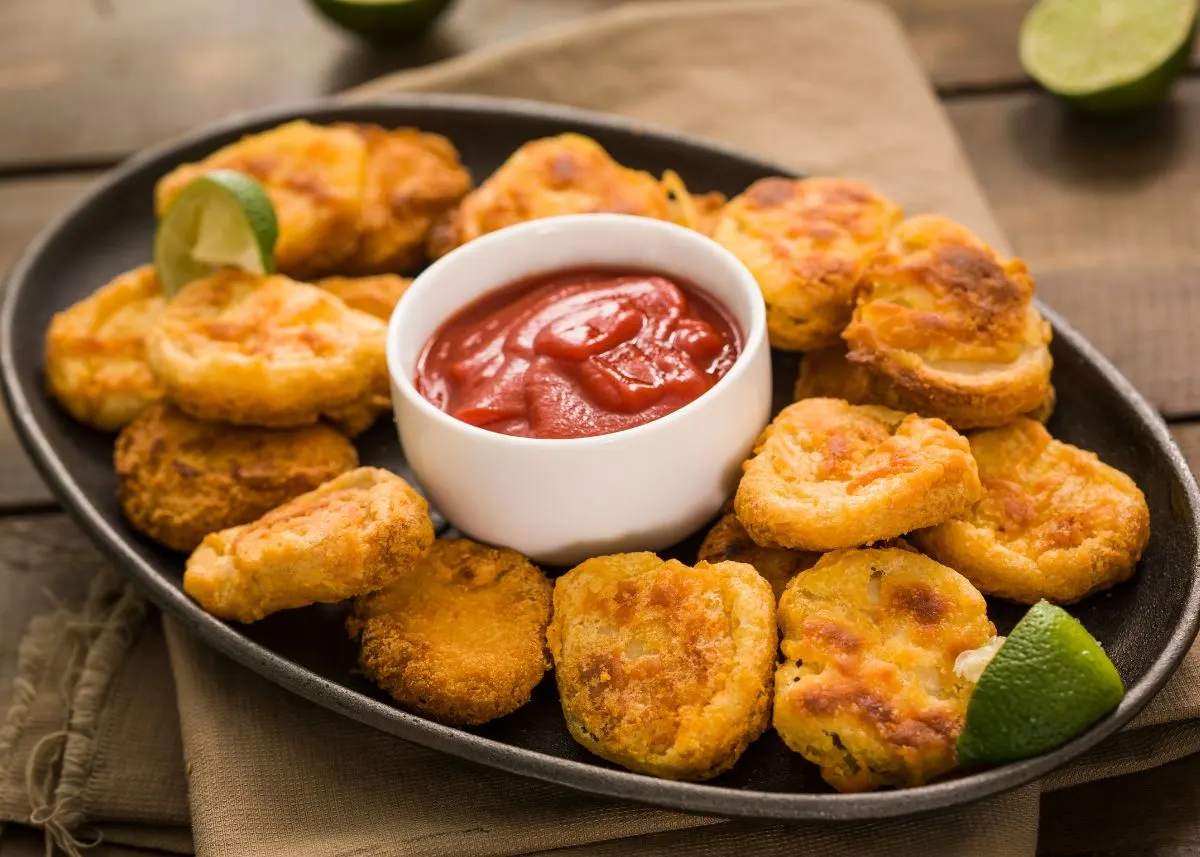 Crispy chicken nuggets with lime wedges and bowl of ketchup on a black serving platter.