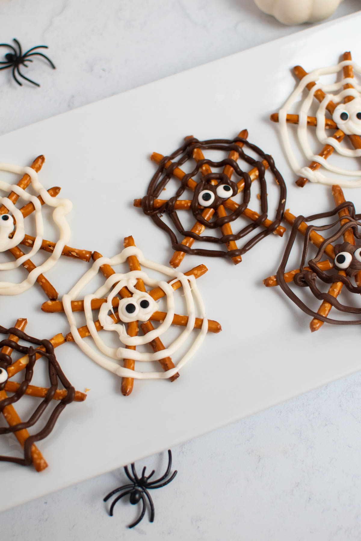 Chocolate pretzel spider webs with candy eyes on white platter.