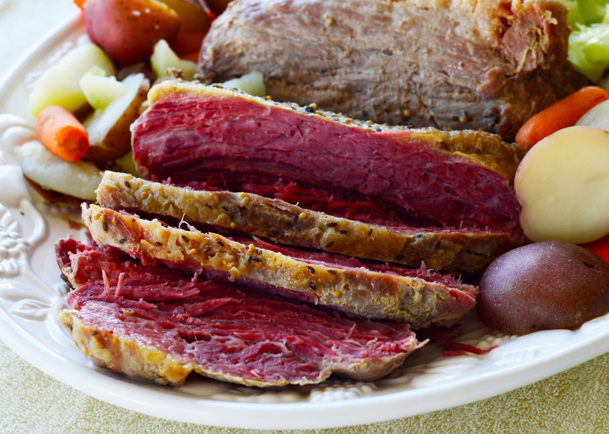 Sliced corned beef with root vegetables on a large white serving platter.