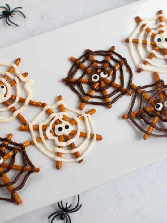 Chocolate pretzel spider webs with candy eyes on white platter.