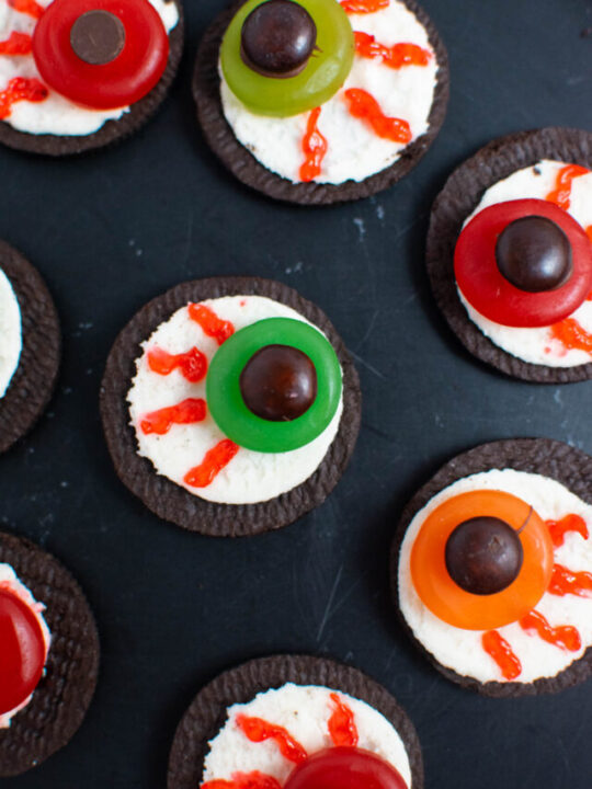 Oreo eyeballs with colorful gummy candies on black plate.