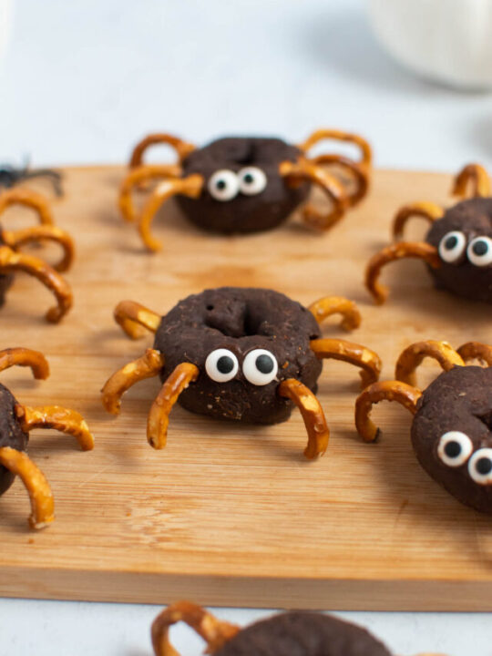 Spider donuts with pretzel legs and candy eyes on wood cutting board.