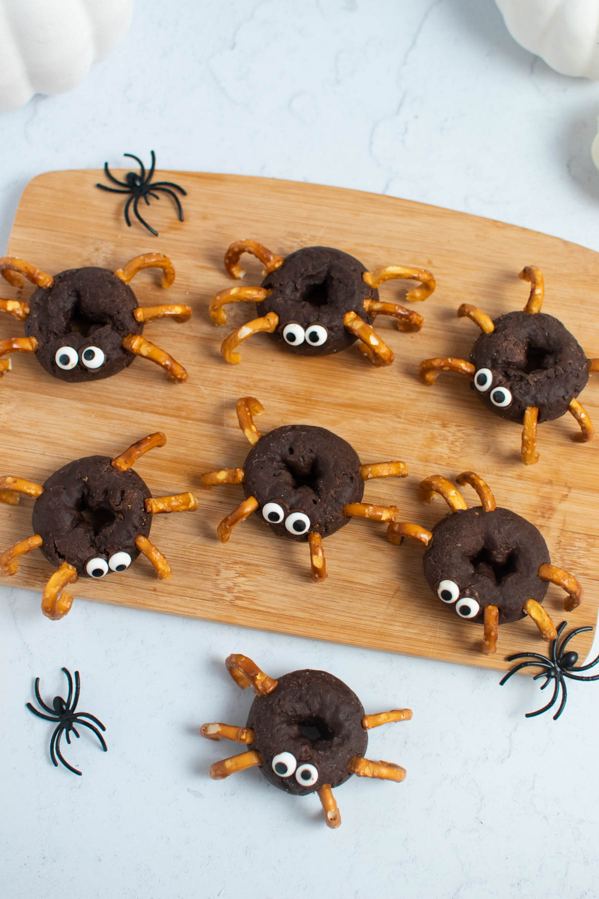 Seven donut spiders on wood cutting board surrounded by plastic spiders.