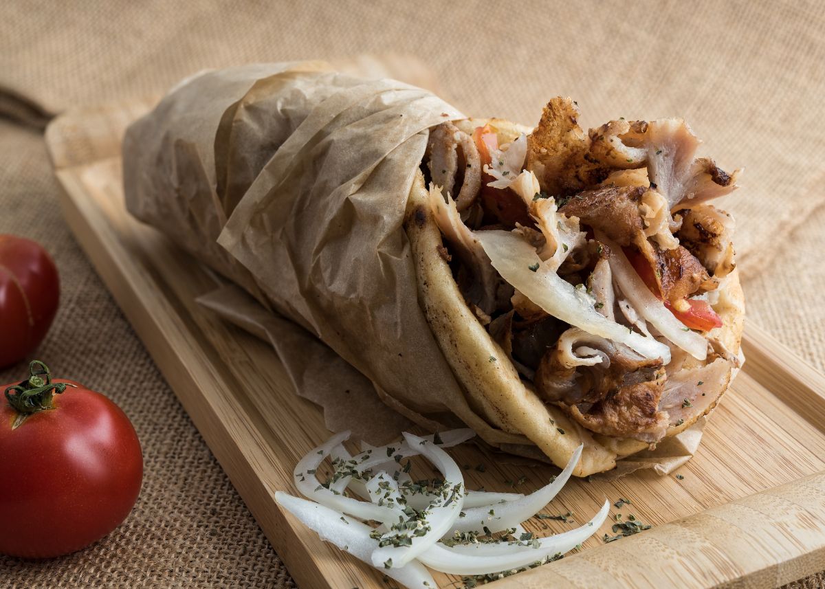 A Greek gyro with tomato and onion wrapped in parchment paper on wood platter.