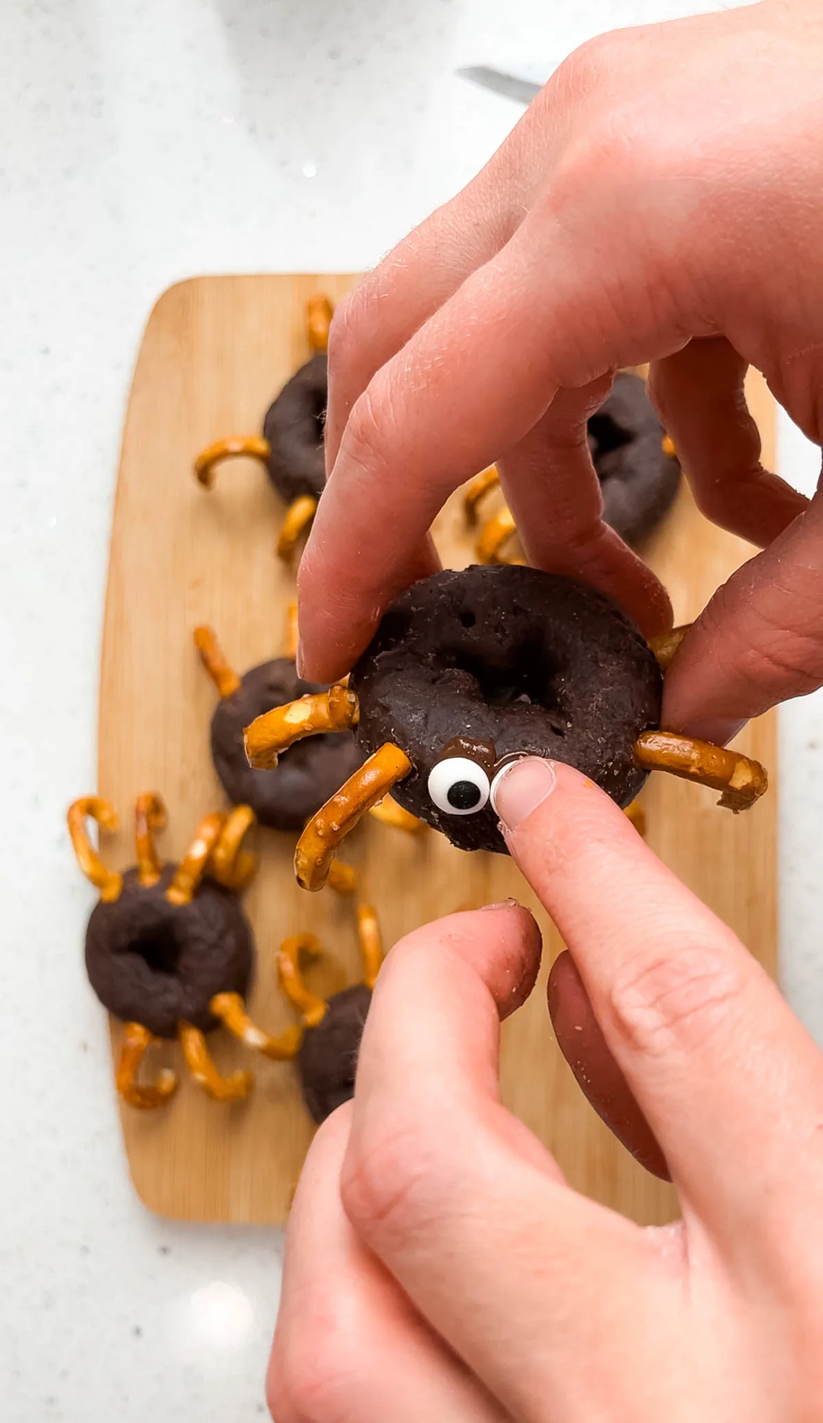 Hands press candy eyes onto mini chocolate donut spider.