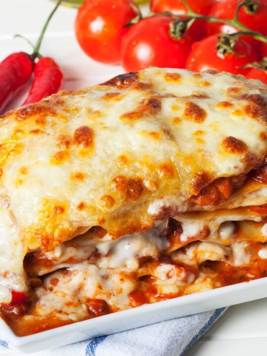 A slice of lasagna on a small rectangular plate next to tomatoes.