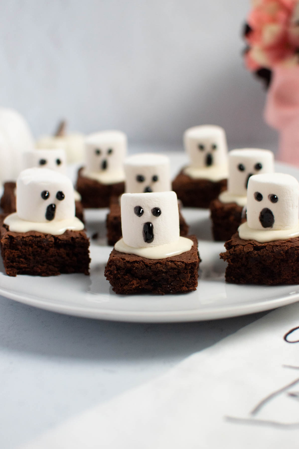 Marshmallow ghost brownies with gel faces on white platter.