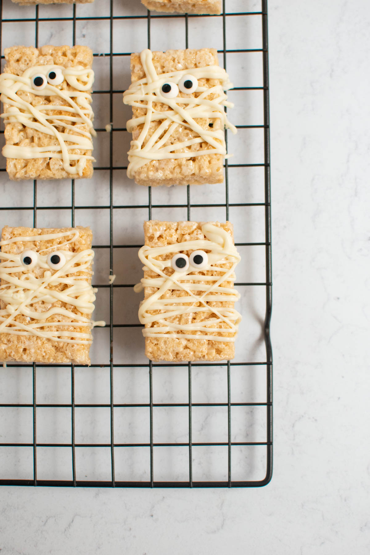 Mummy rice krispie treats with candy eyes on baking rack.