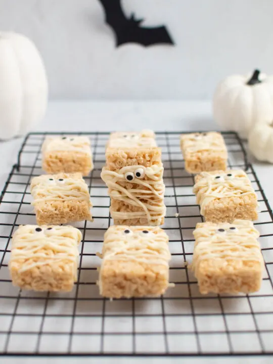Mummy rice krispie treat standing up on baking rack surrounded by other rice krispie treats.