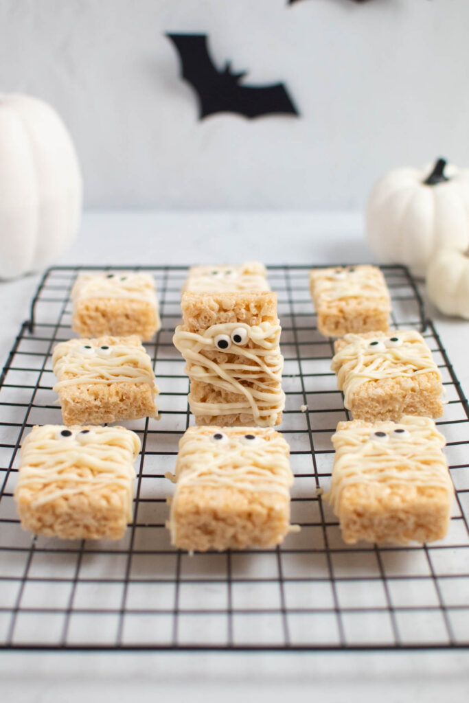 Mummy rice krispie treat standing up on baking rack surrounded by other rice krispie treats.