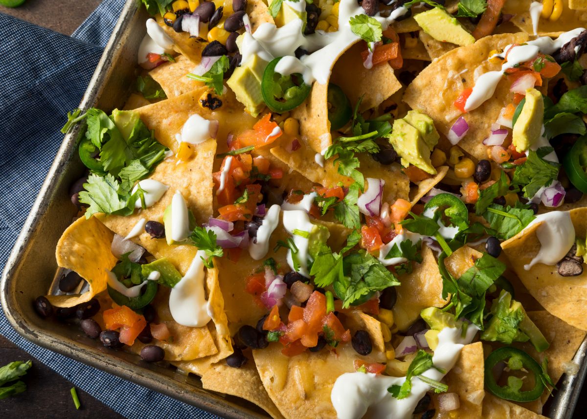 A sheet pan filled with nachos with toppings like sour cream, cheese, cilantro, and avocado.
