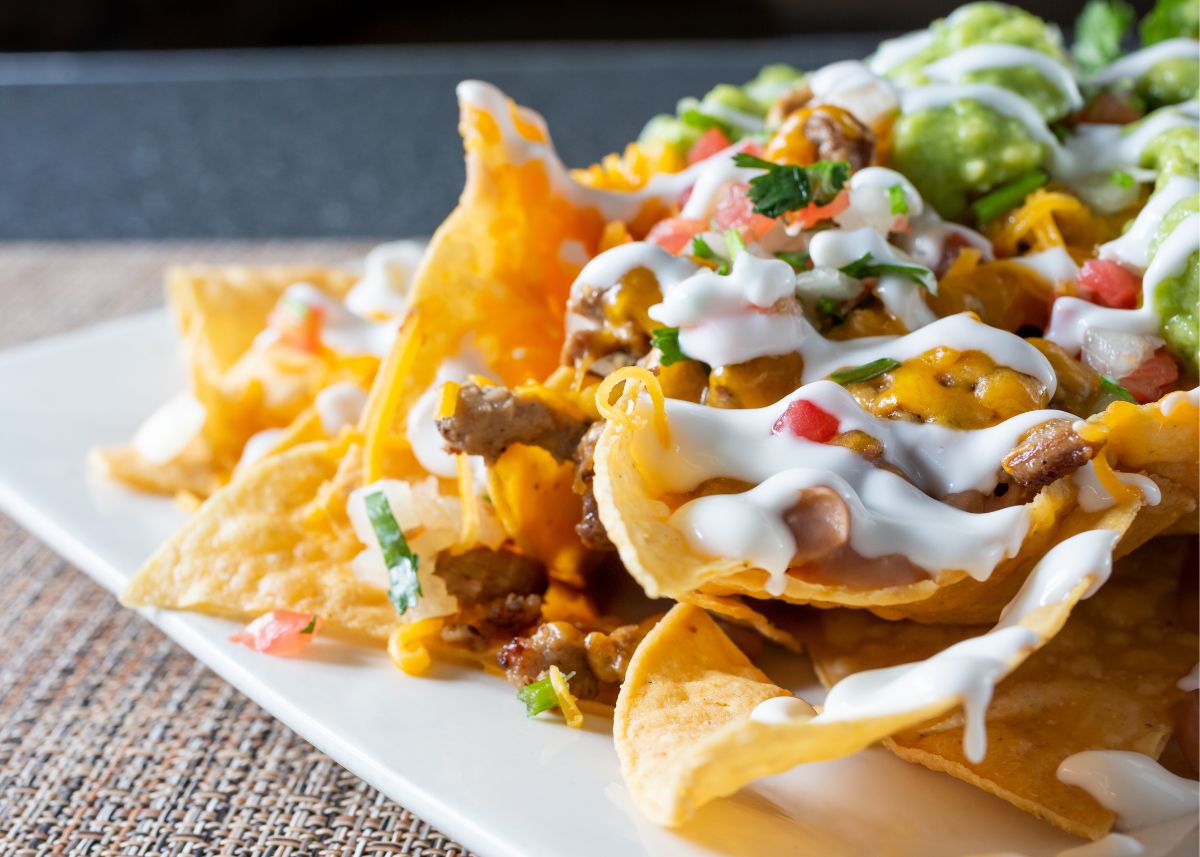 Close up of nachos on a white plate with toppings and sour cream.