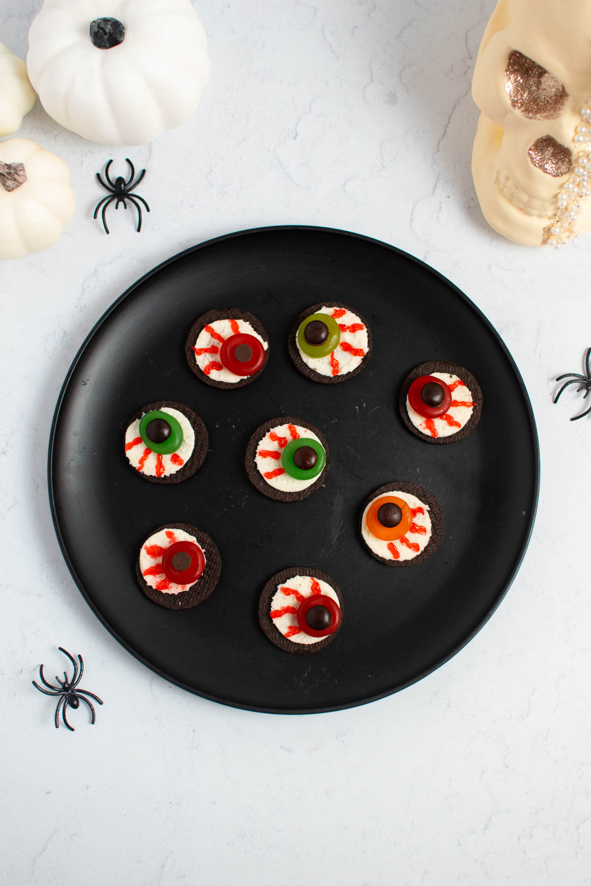 Oreo eyeball cookies on black plate surrounded by plastic spiders, pumpkins, and skull head.
