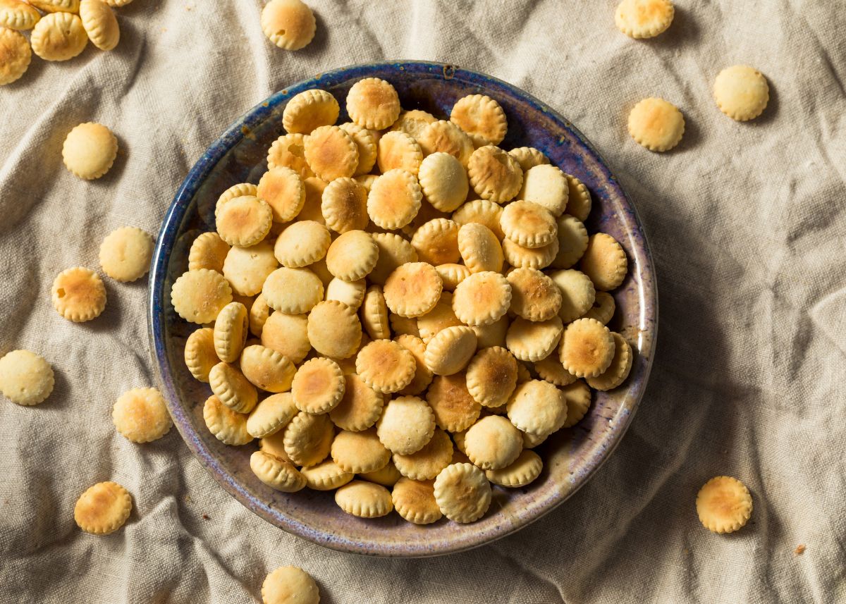 A large blue and tan bowl filled with oyster crackers sitting on a gray cloth.