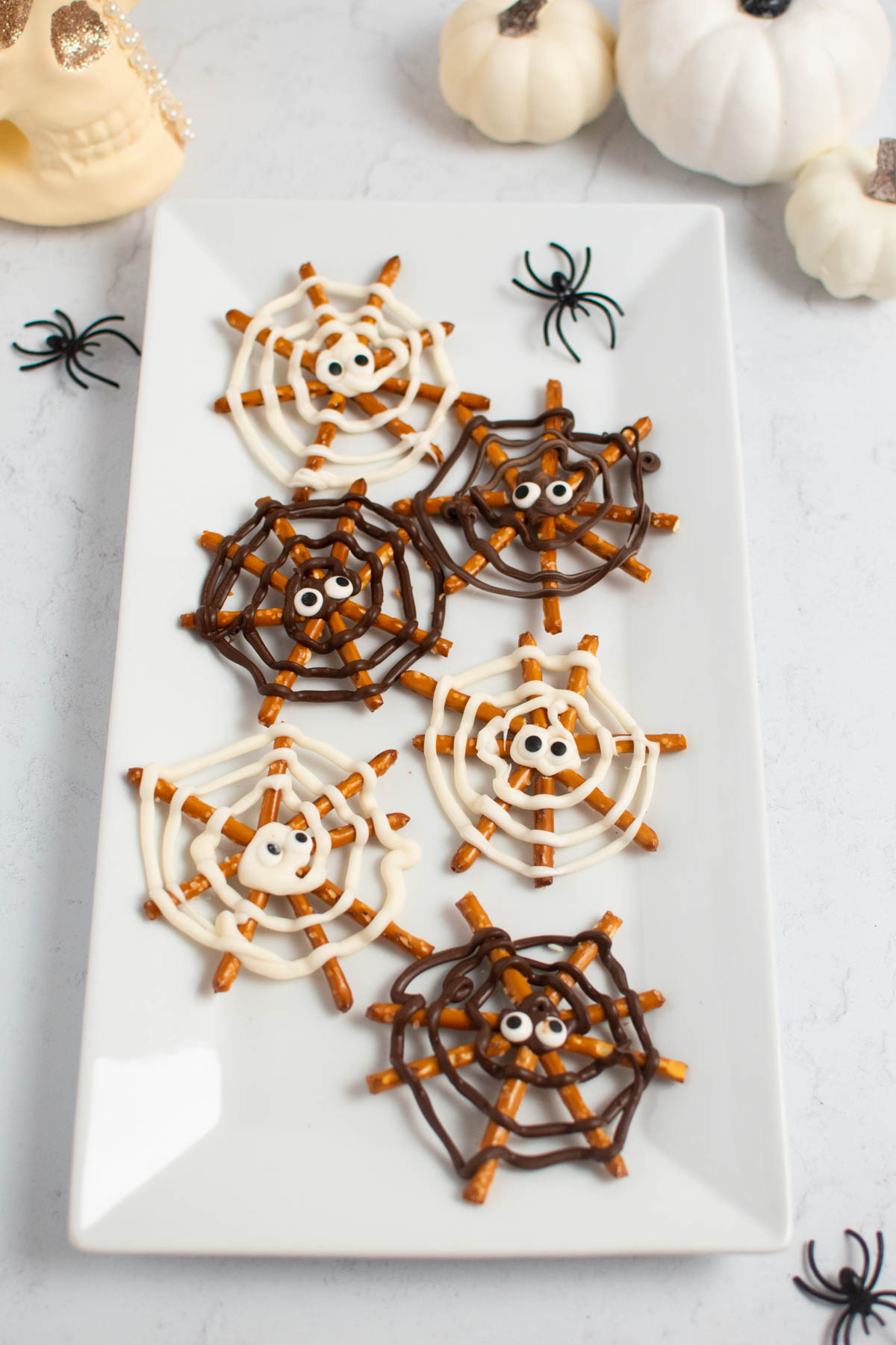 Pretzel spider webs with candy eyes on platter with plastic spiders and pumpkins.