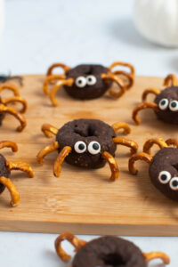 Spider donuts with pretzel legs and candy eyes on wood cutting board.