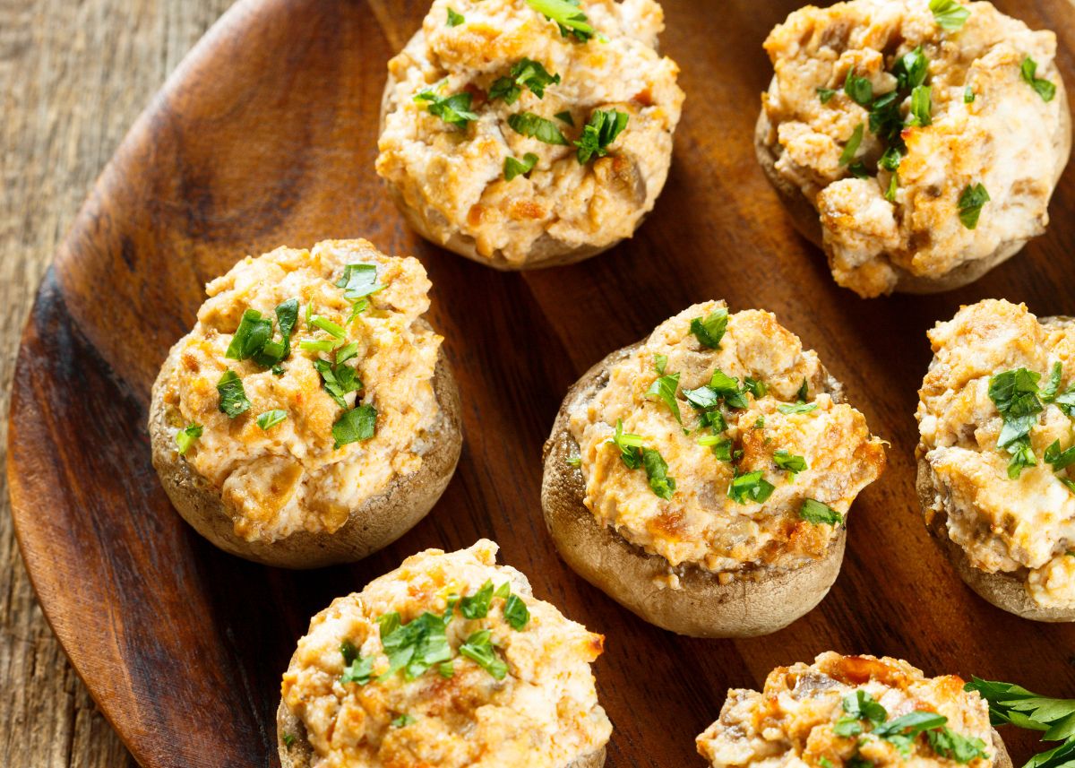 Cheesy stuffed mushrooms with green garnish on a large wooden platter.