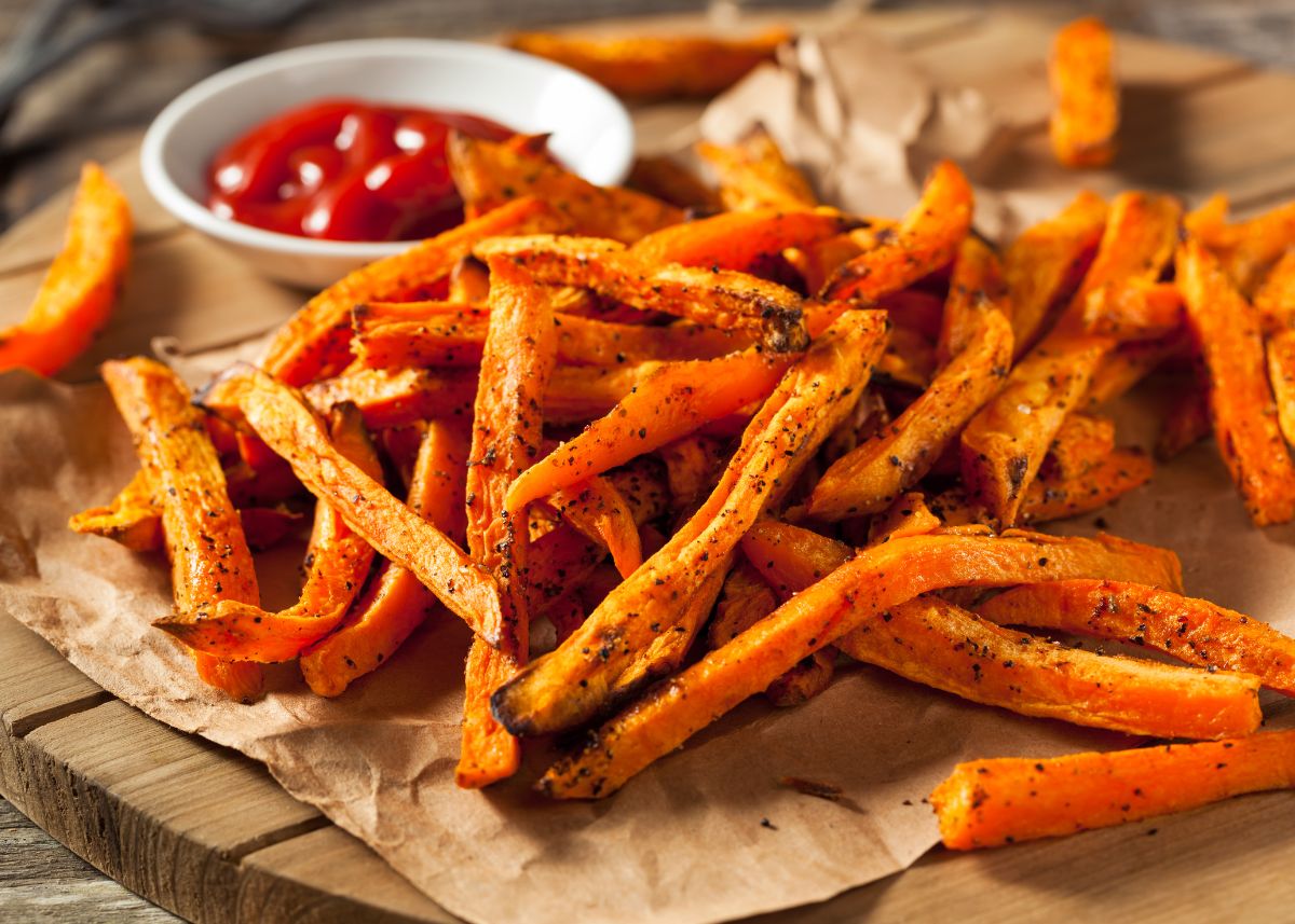 Large pile of sweet potato fries on parchment paper with ketchup.