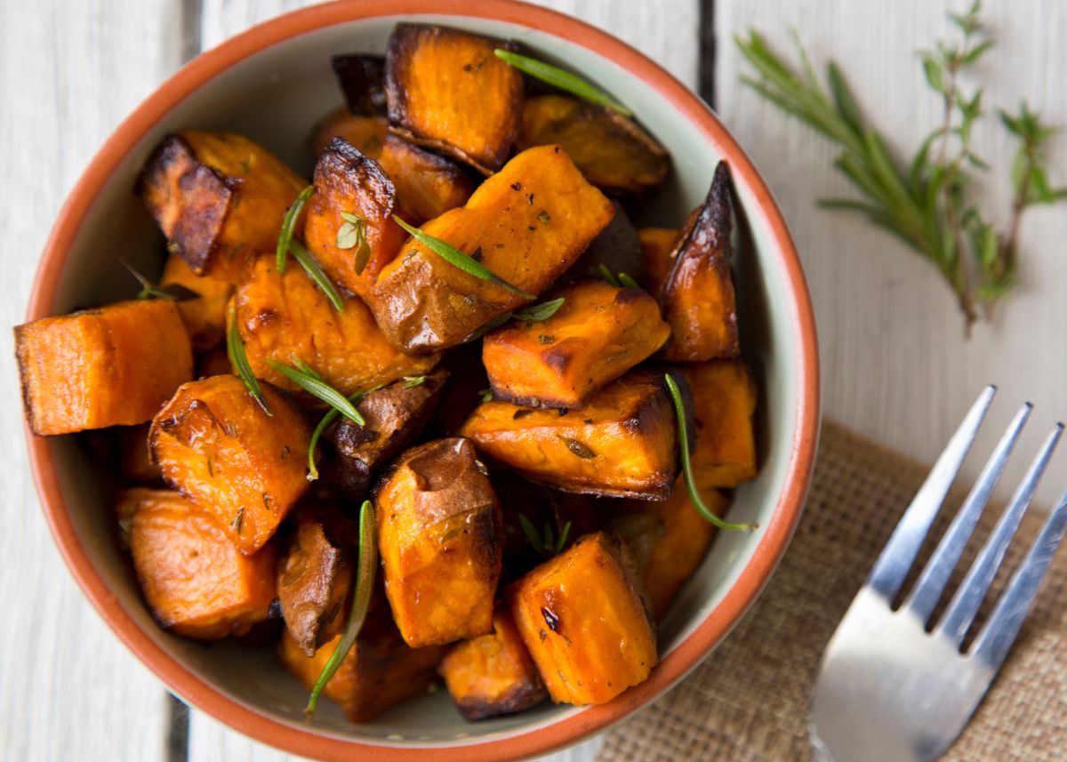 Diced and roasted sweet potatoes with herbs in a bowl on wooden table.