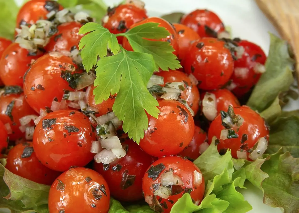 Cherry tomato salad with herbs, onion, and green garnish over bed of lettuce.