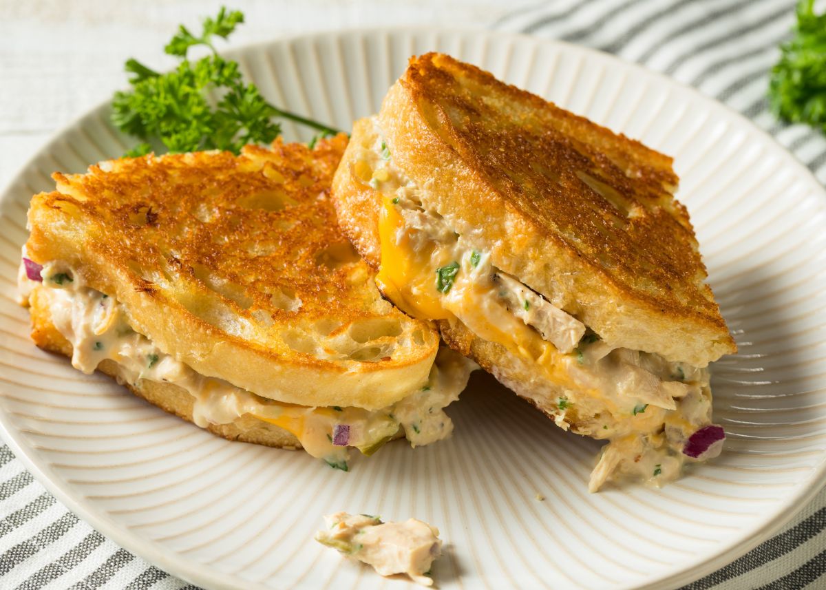 Two cheesy tuna melt sandwiches on a white plate with green garnish.