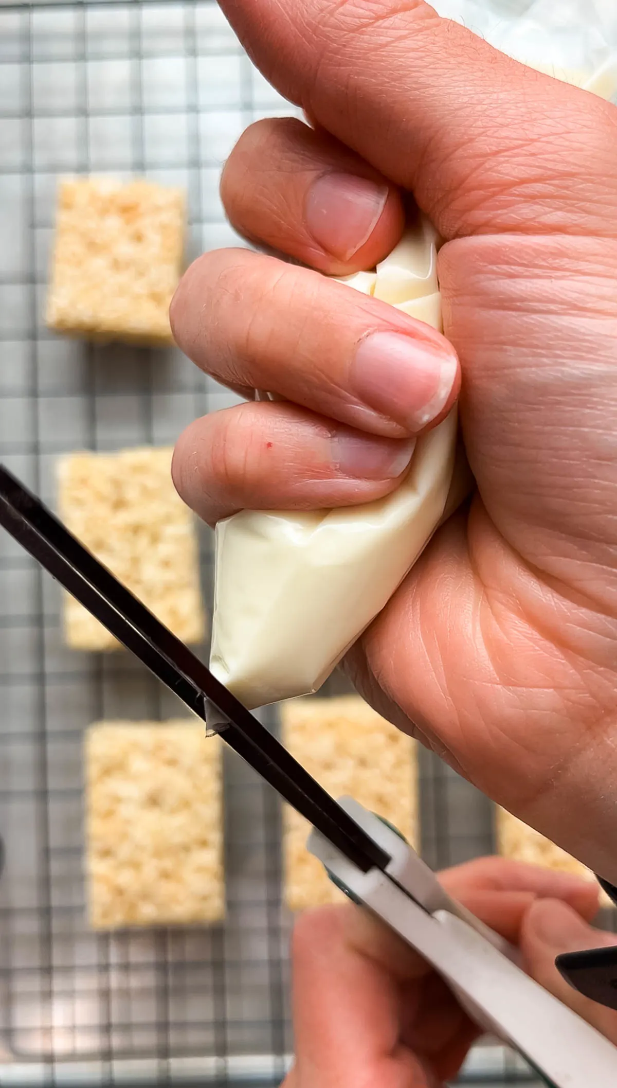 Woman cuts piping bag full of white chocolate with pair of scissors.