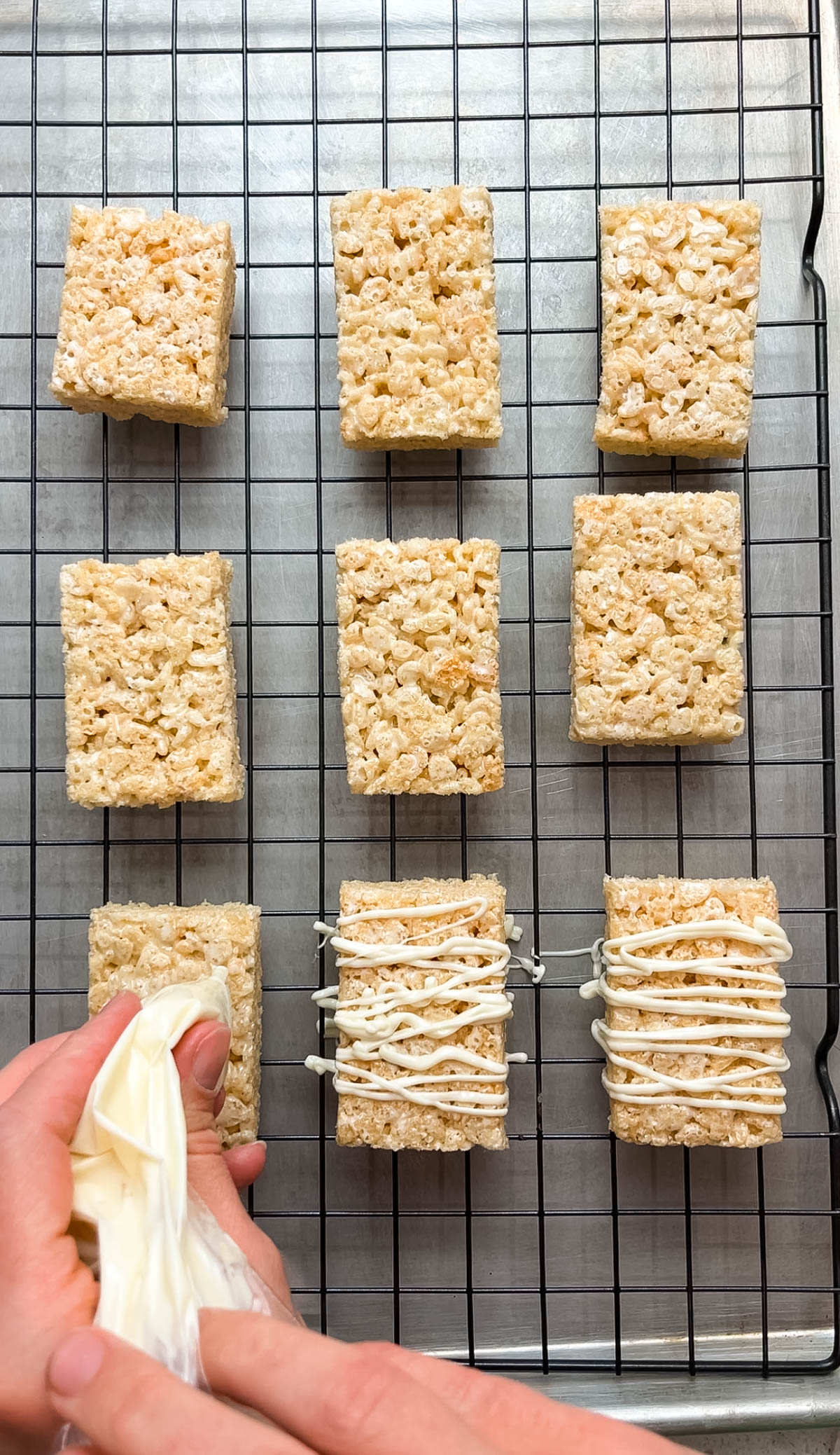 Woman drizzles white chocolate from a piping bag onto rice krispie treats.
