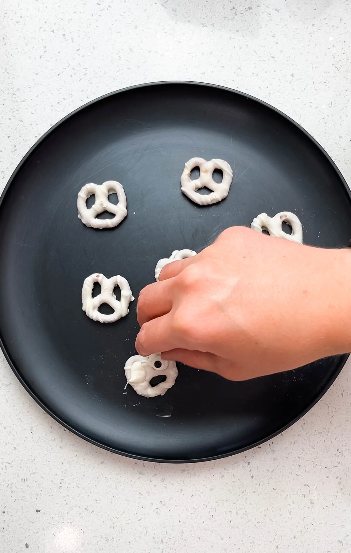 Woman places candy eye on white chocolate pretzels with melted white chocolate.