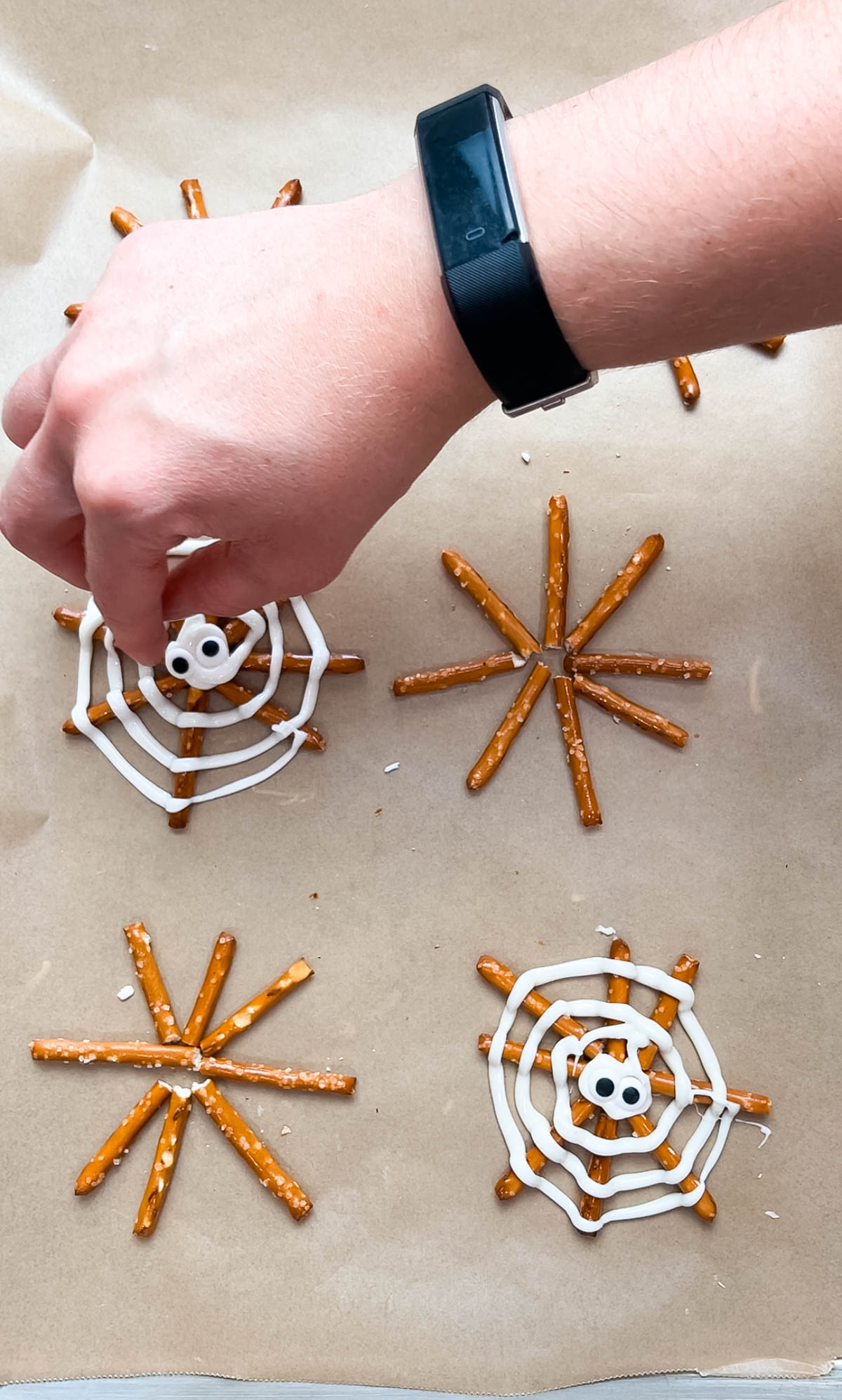 Woman places candy eyes on chocolate pretzel spider webs.