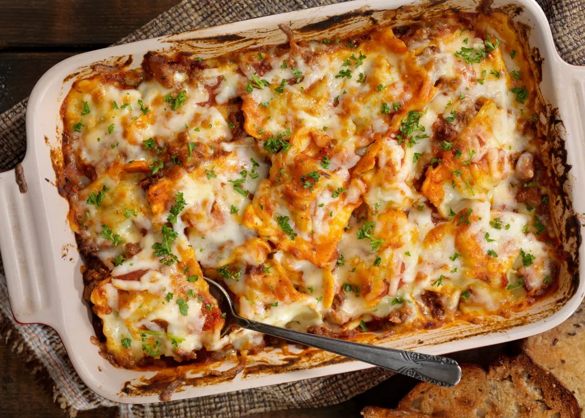 Baked lasagna in a casserole dish with green garnish and a metal spoon.