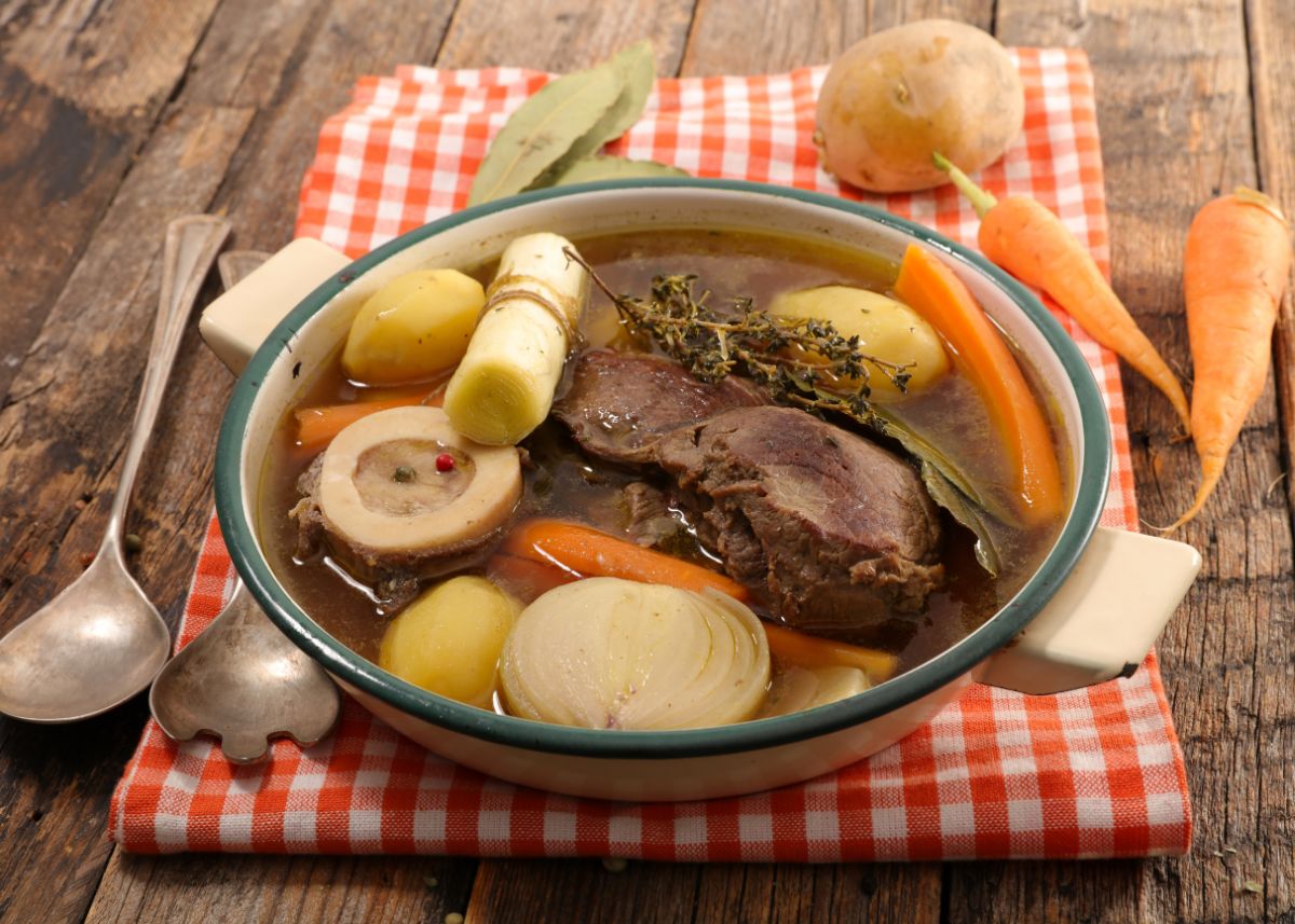 A large bowl of beef broth ingredients including meat, vegetables, and aromatics.