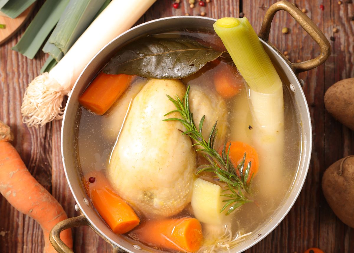 A large stock pot with a whole chicken and vegetables to make chicken broth.