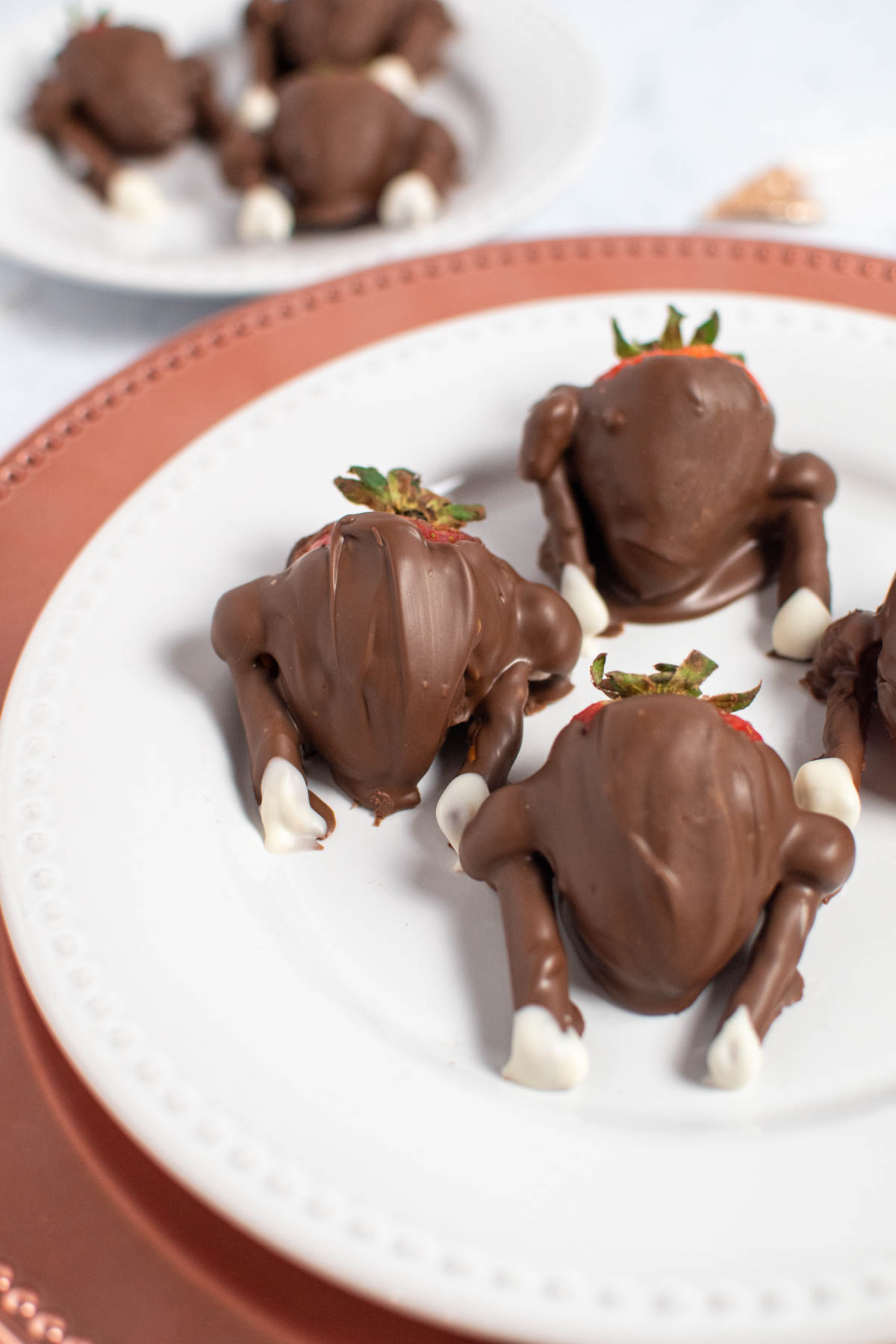 Four chocolate covered strawberry turkeys on white plate with more in background.
