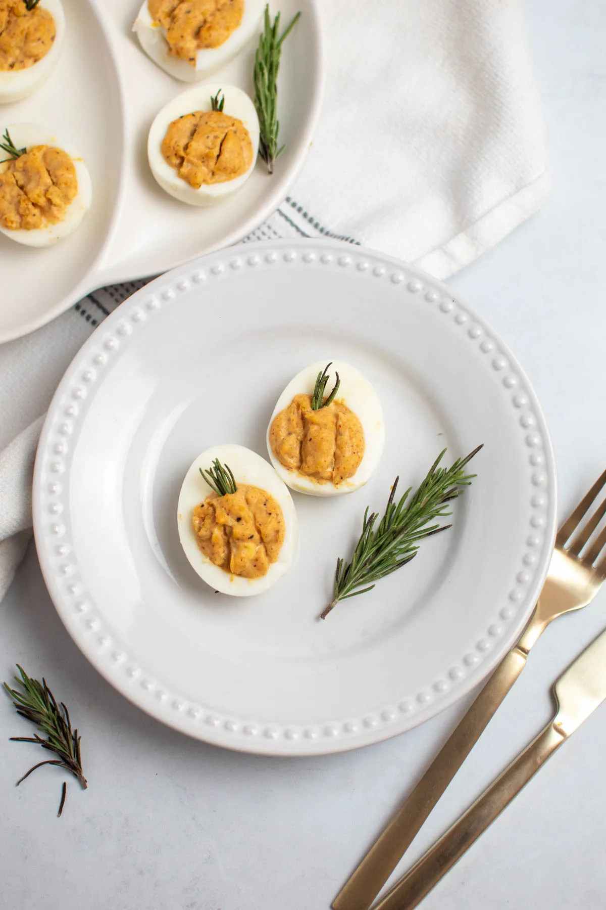 Two Thanksgiving deviled eggs on a white plate with sprig of fresh rosemary.