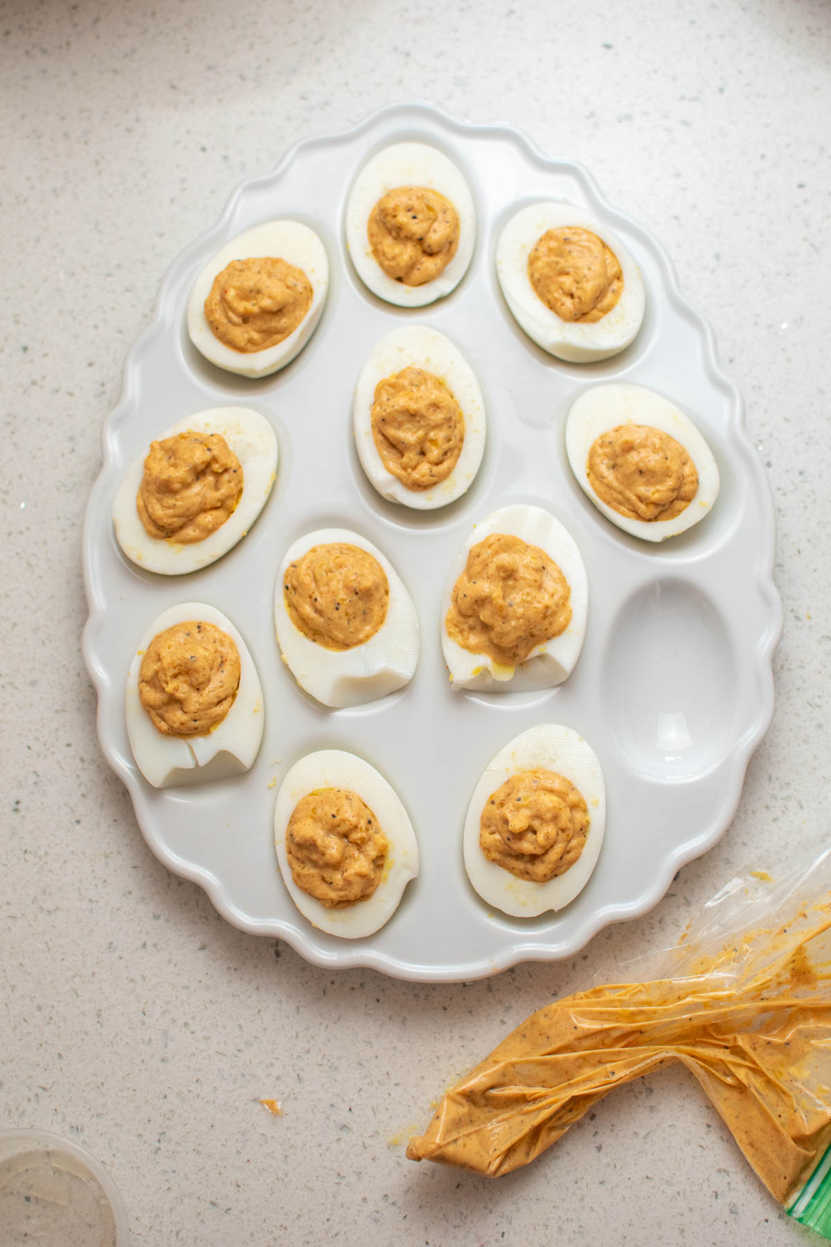 Deviled eggs on white egg-shaped platter with bag of filling nearby.