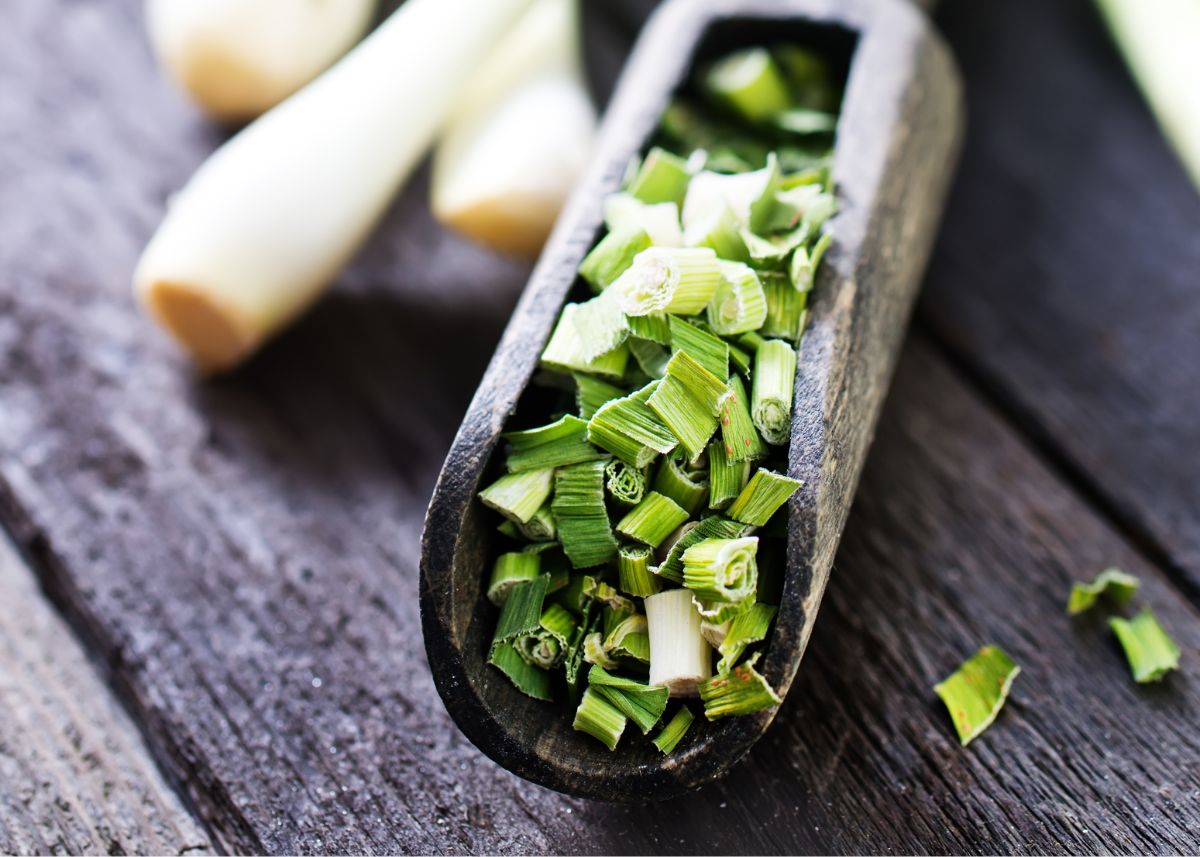 A rustic wooden ladle filled with dried green onion next to fresh green onion on a table.